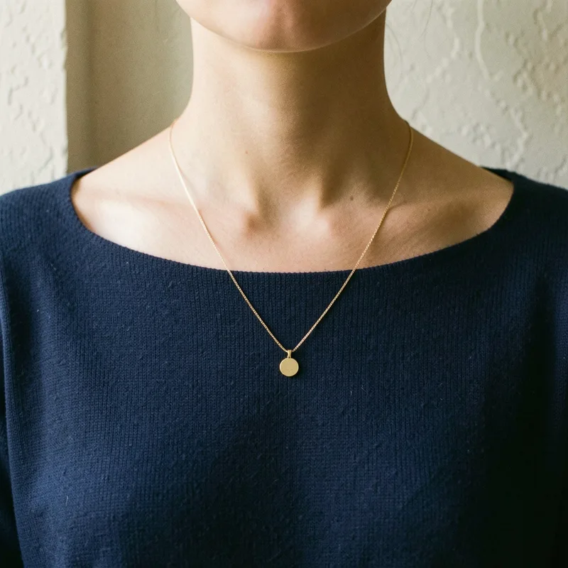Femme portant un pull à col bateau et une chaîne fine à pendentif discret, lumière naturelle